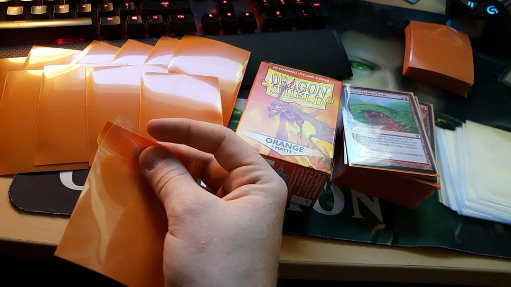 Orange matte dragon shield sleeves, hand holding one that is torn