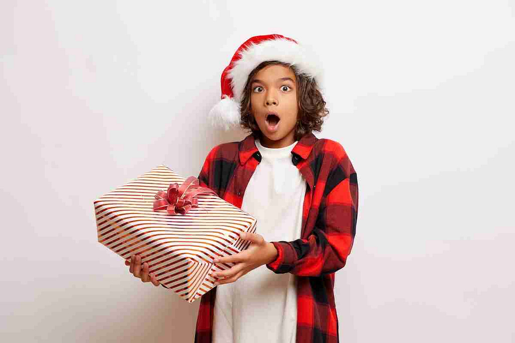 Boy in Santa hat holding present, looking surprised