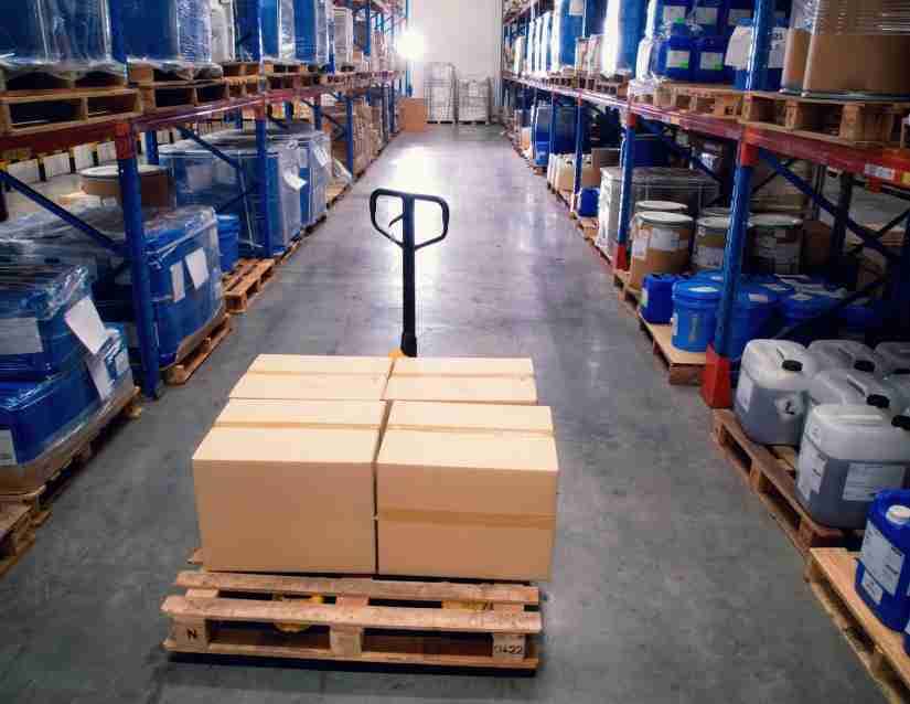 A warehouse aisle with a floor jack in the middle with a pallet and boxes on it