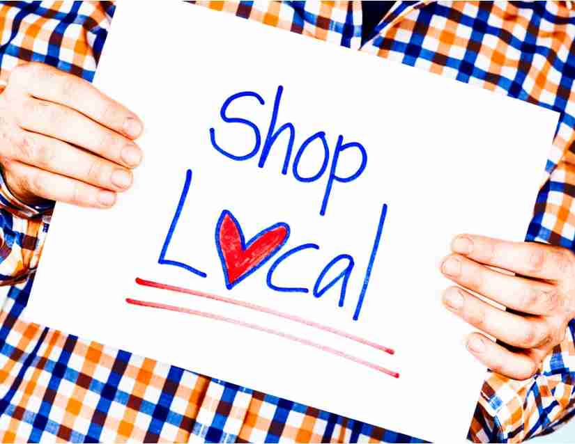 Person in plaid shirt holding a sign that says "Shop Local."
